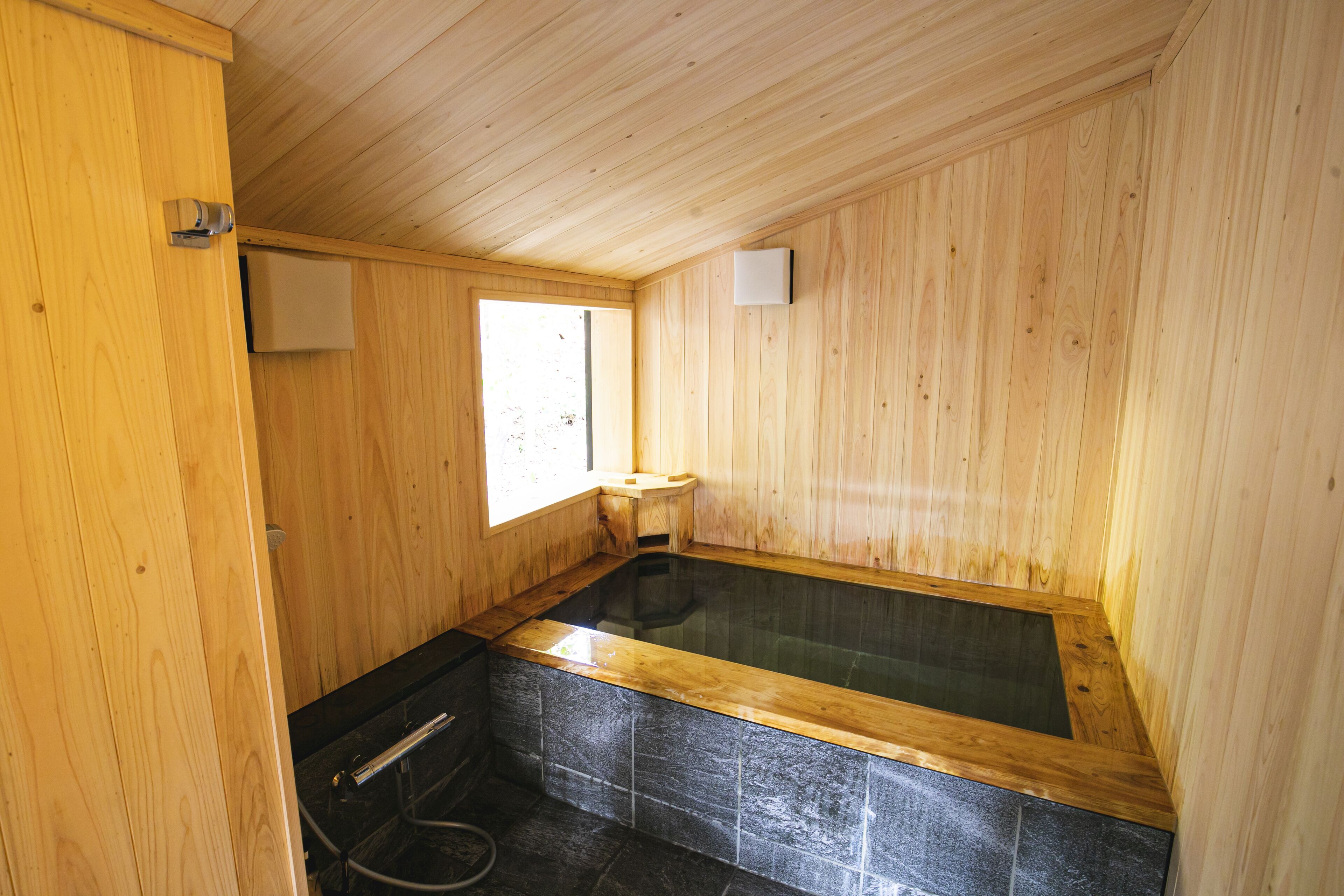 Een houten interieur met een ligbad van steen, houten wanden en een raam.