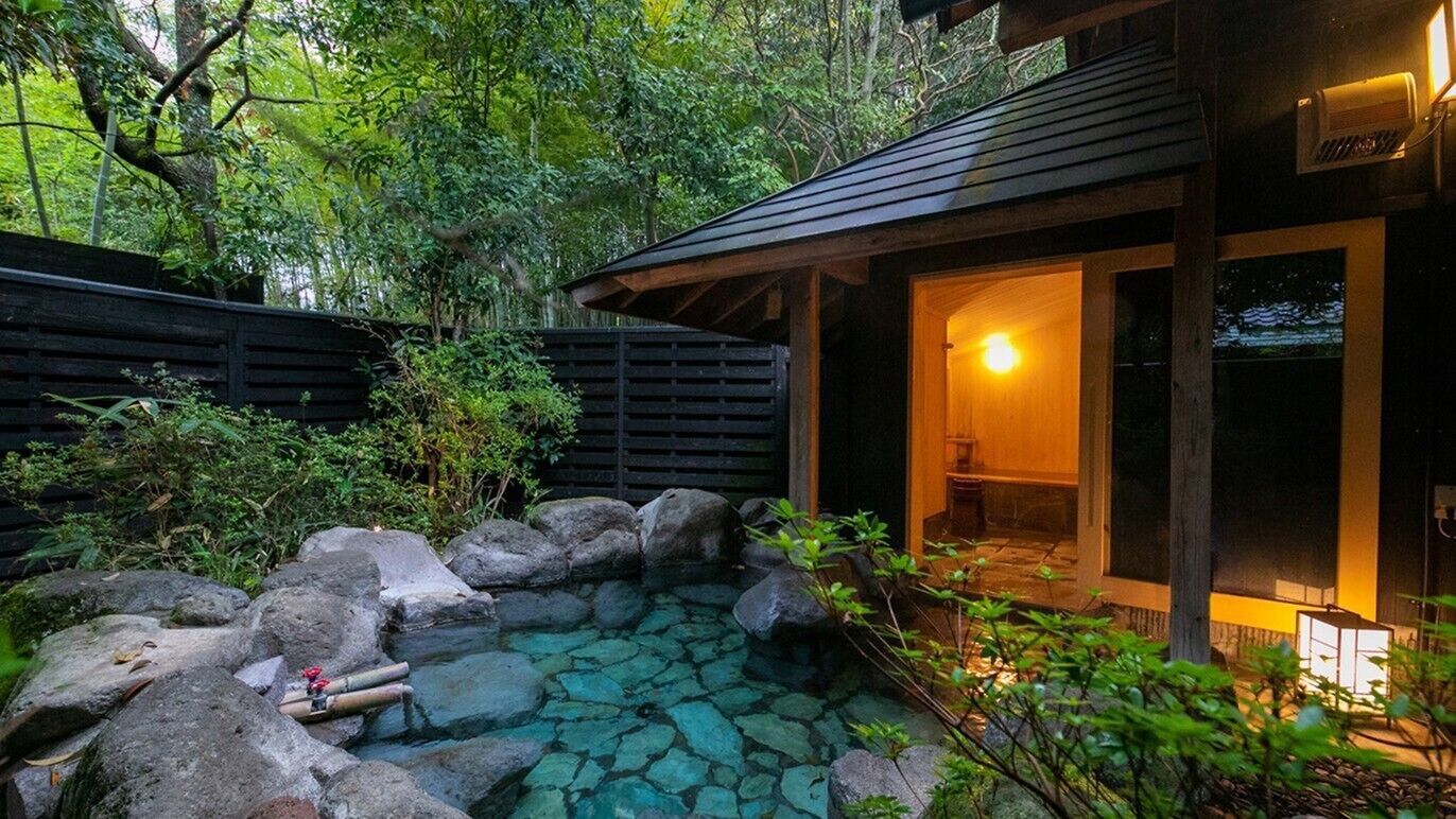 A traditional Japanese-style building with a stone pond, wooden deck, and a lit interior.