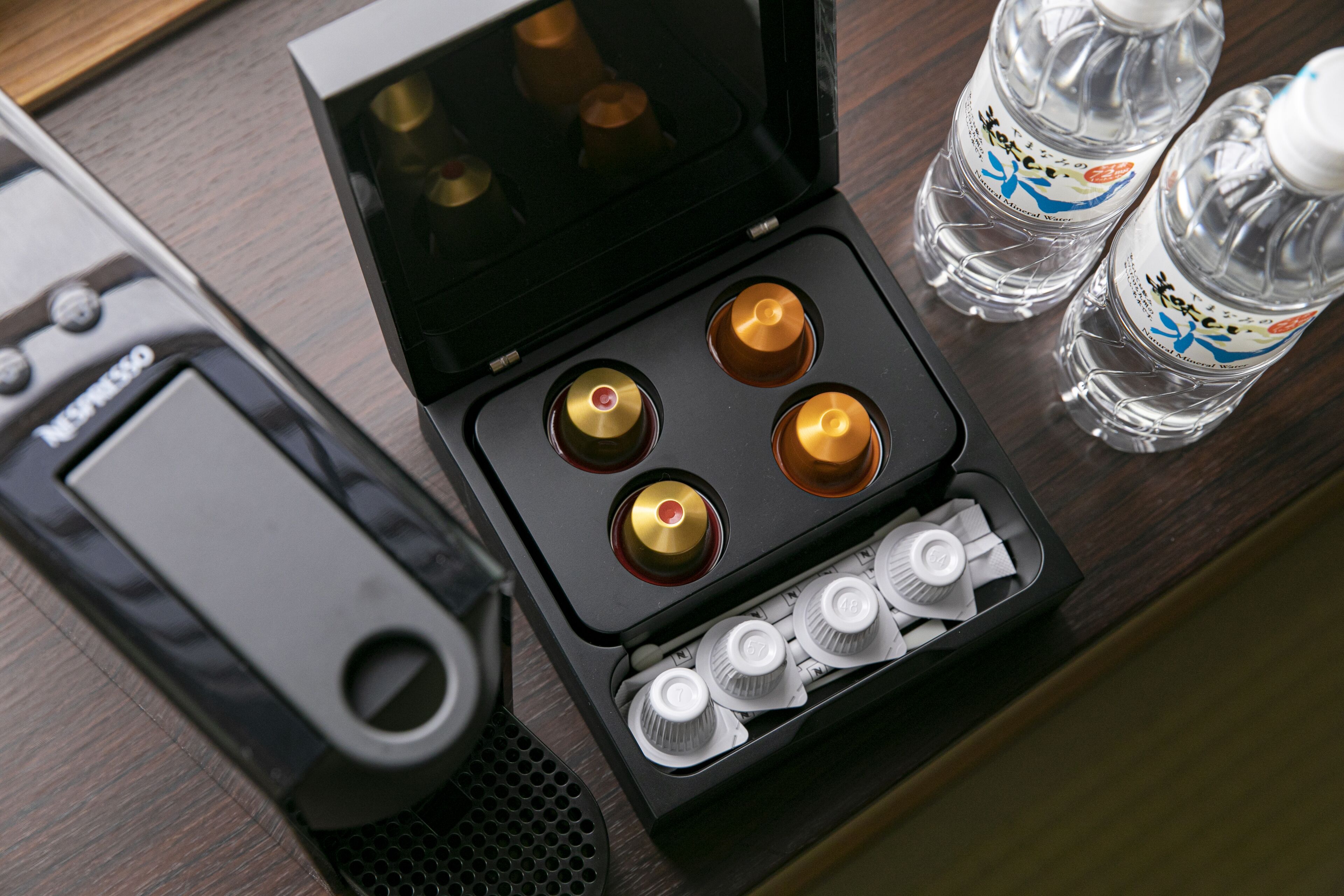 A coffee machine with four coffee pods and two bottles of water on a wooden surface.