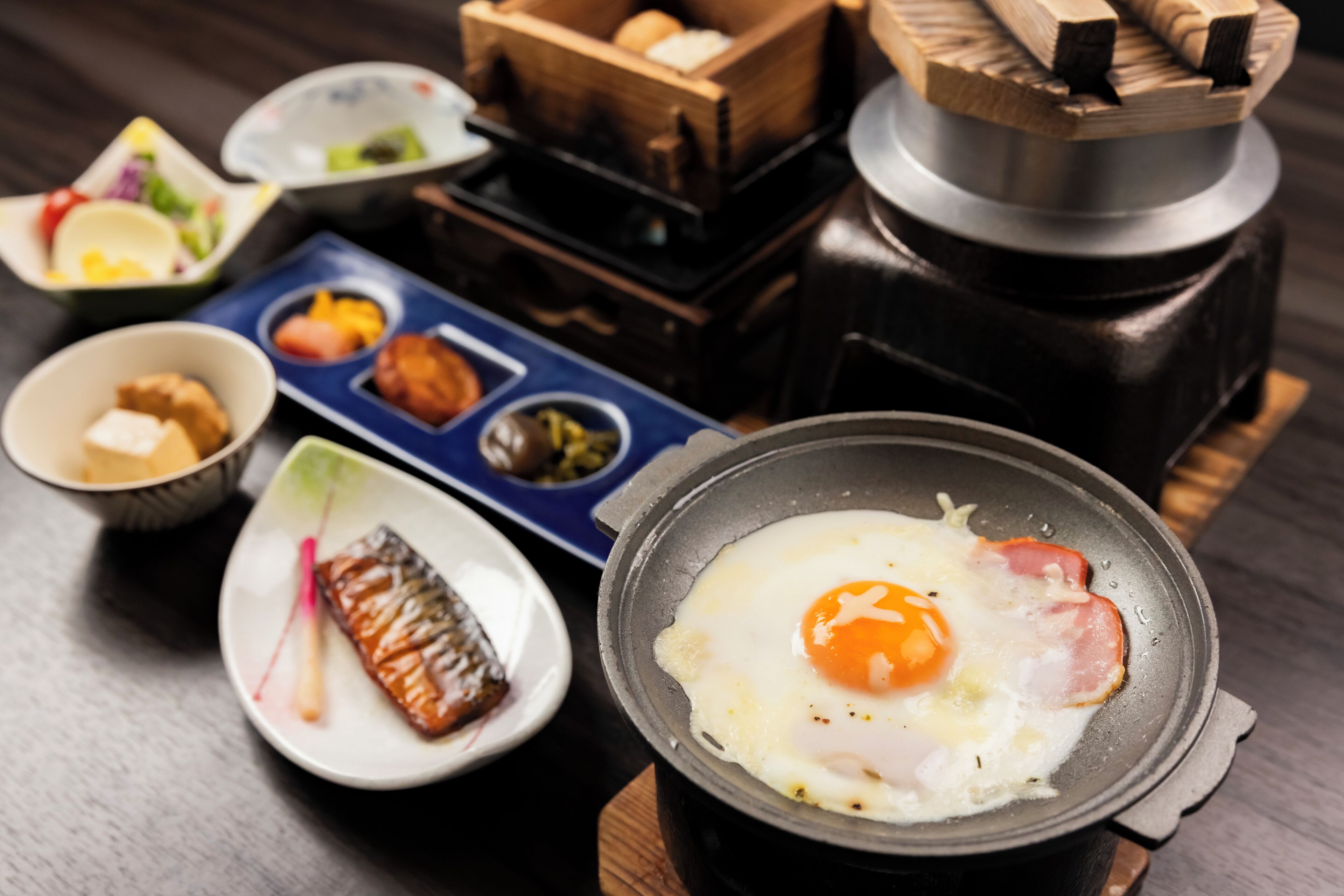 A table with a variety of dishes including a fried egg, a piece of meat, and several small bowls containing different foods.
