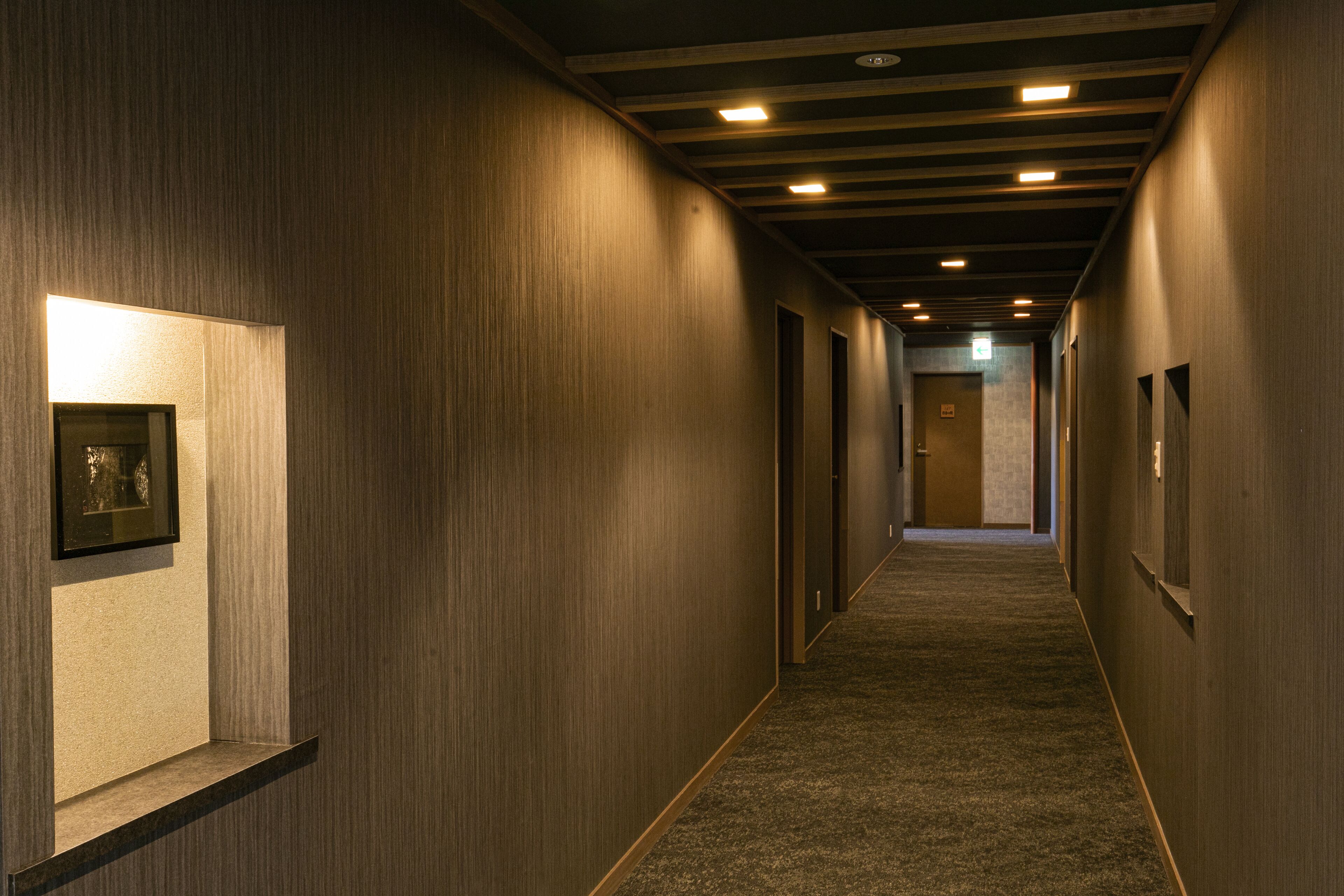 A hallway with wooden walls, framed artwork, and recessed lighting.