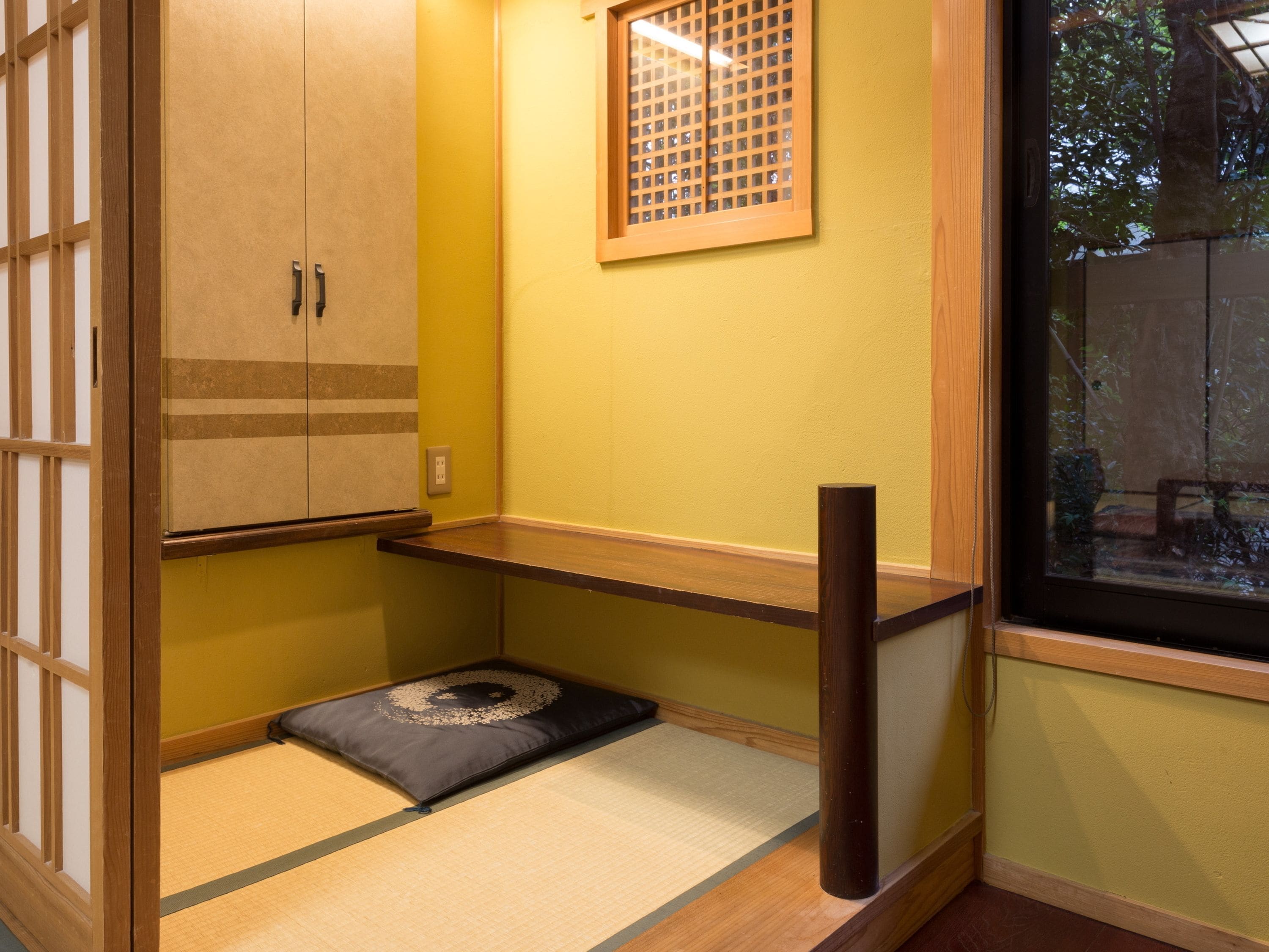Una habitación japonesa tradicional con suelo de tatami, un estante de madera bajo, una puerta corredera y un ventanal con diseño de celosía.