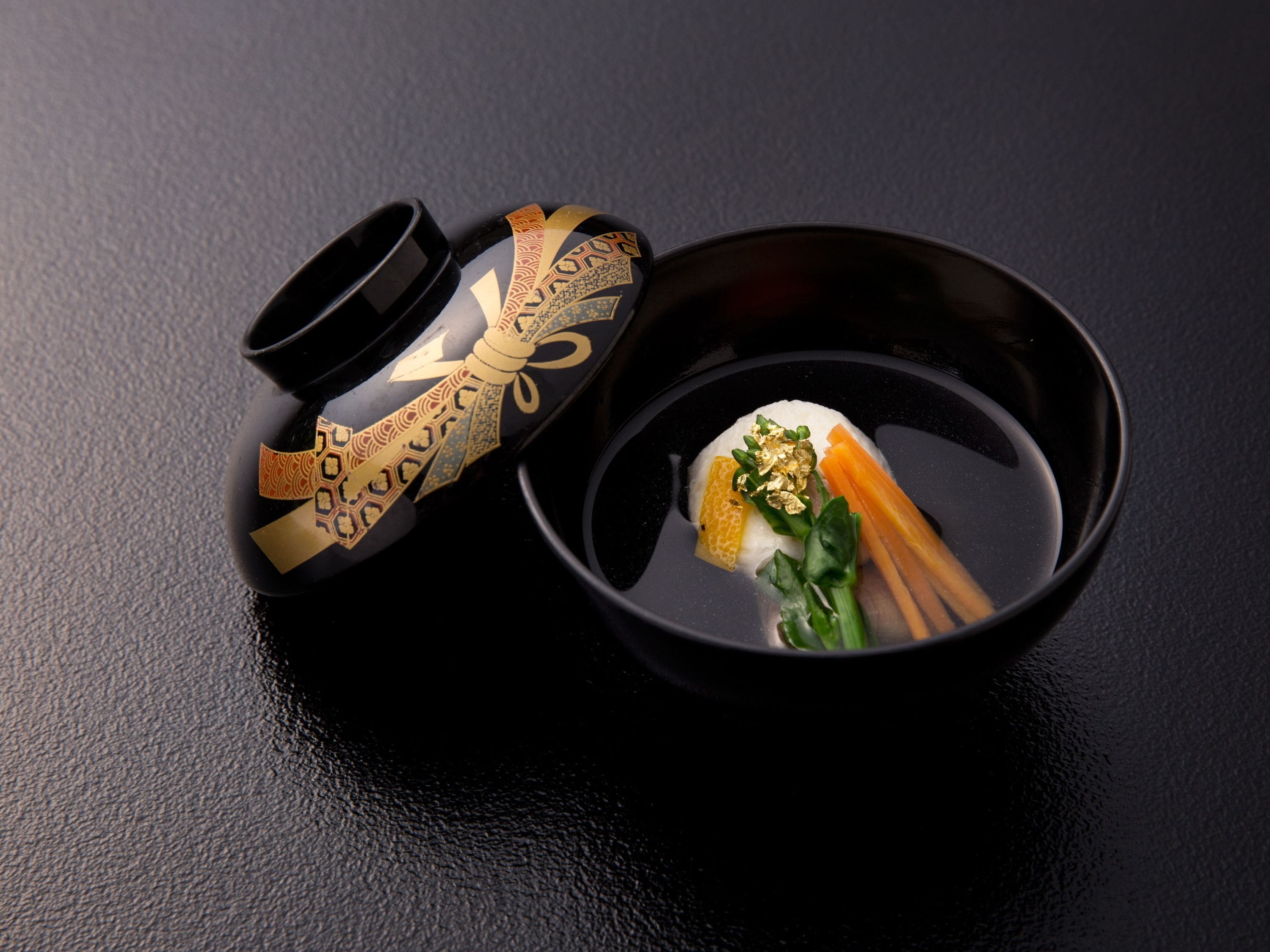 A black bowl with a spoon, containing a white substance, a slice of orange, and green leafy vegetables.