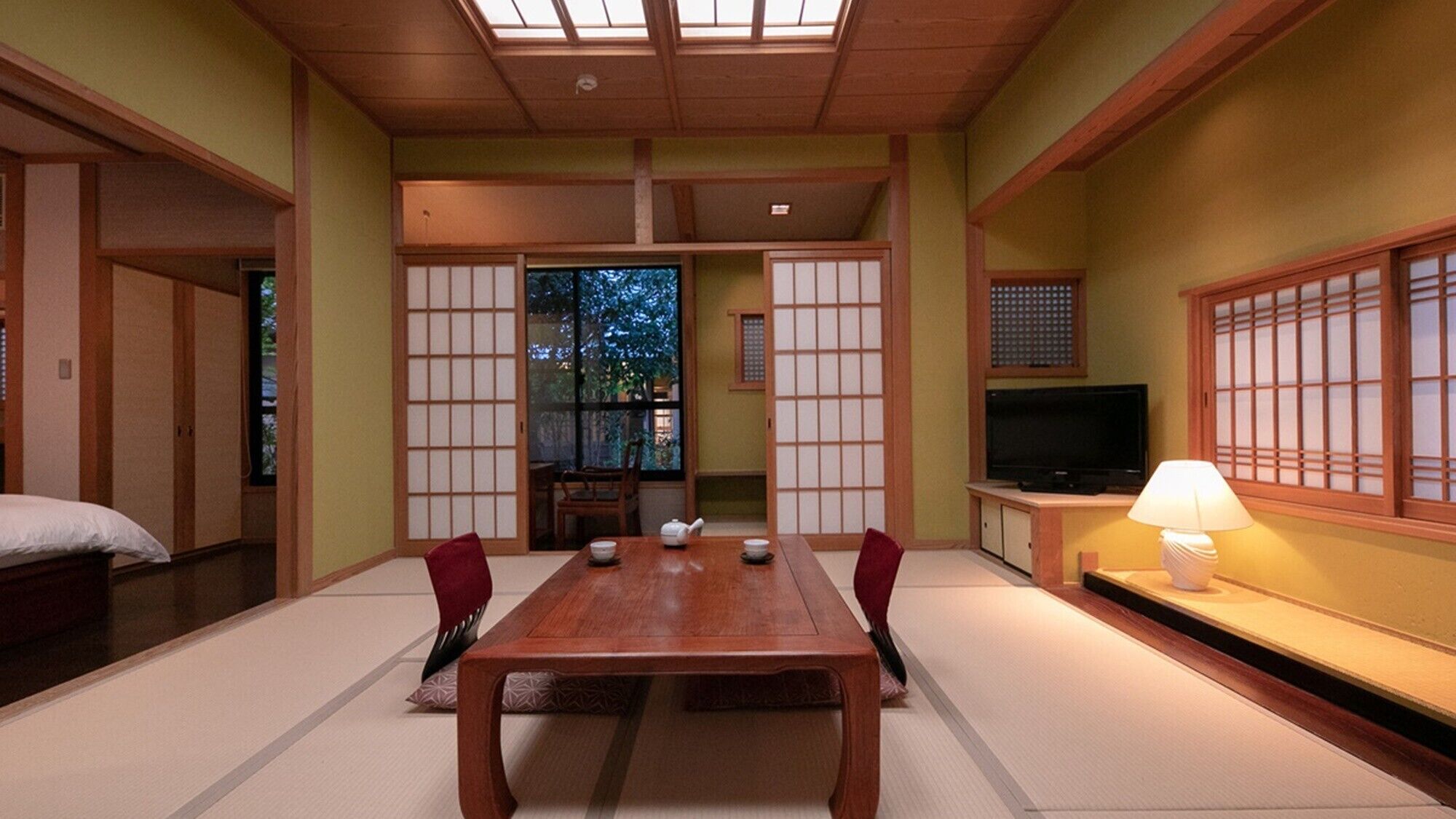 Een traditionele Japanse kamer met tatami vloeren, een lage tafel met stoelen, een televisie en schuifdeuren.