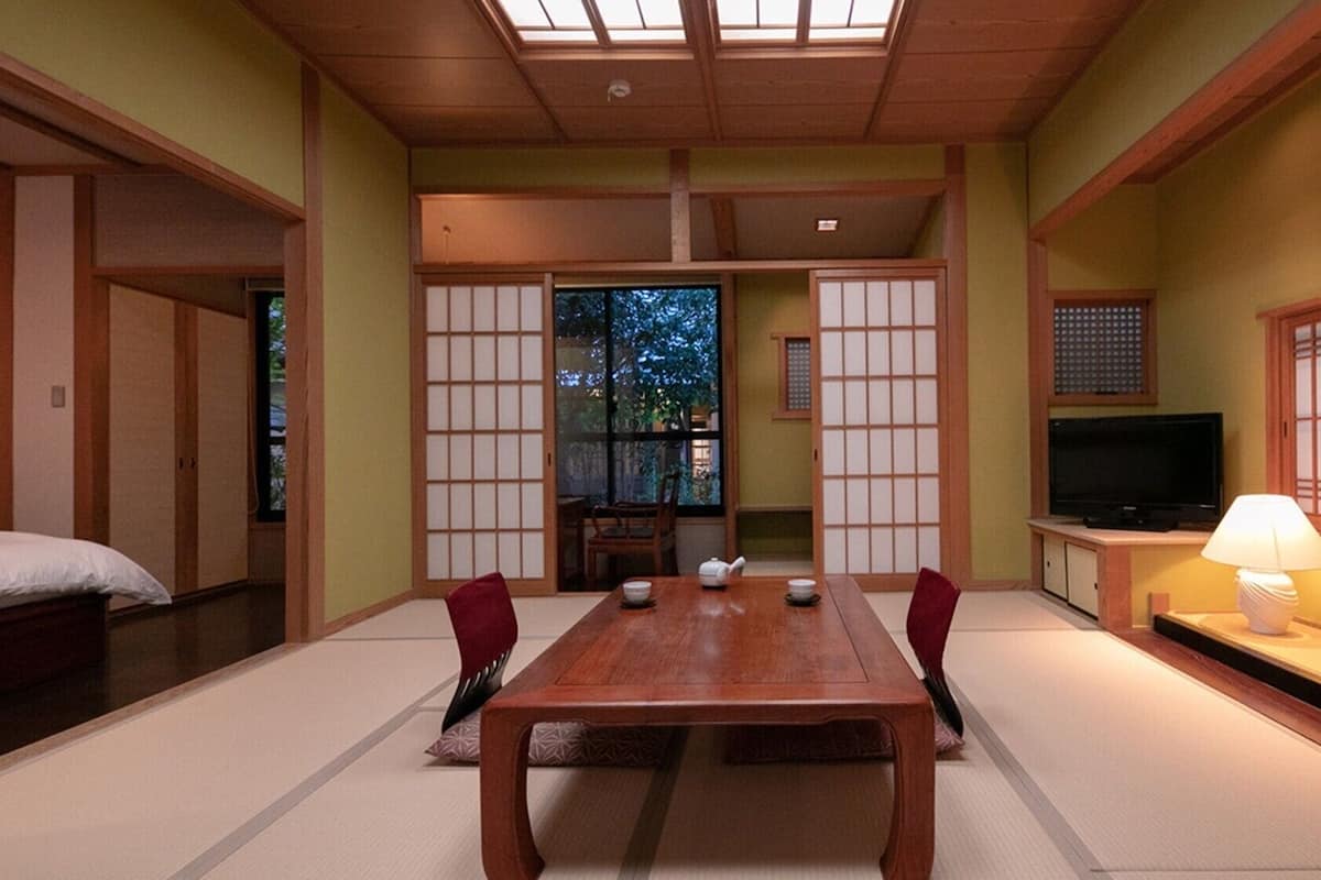 Una habitación de estilo japonés tradicional con suelo de tatami, una mesa baja con sillas, un televisor y puertas correderas.