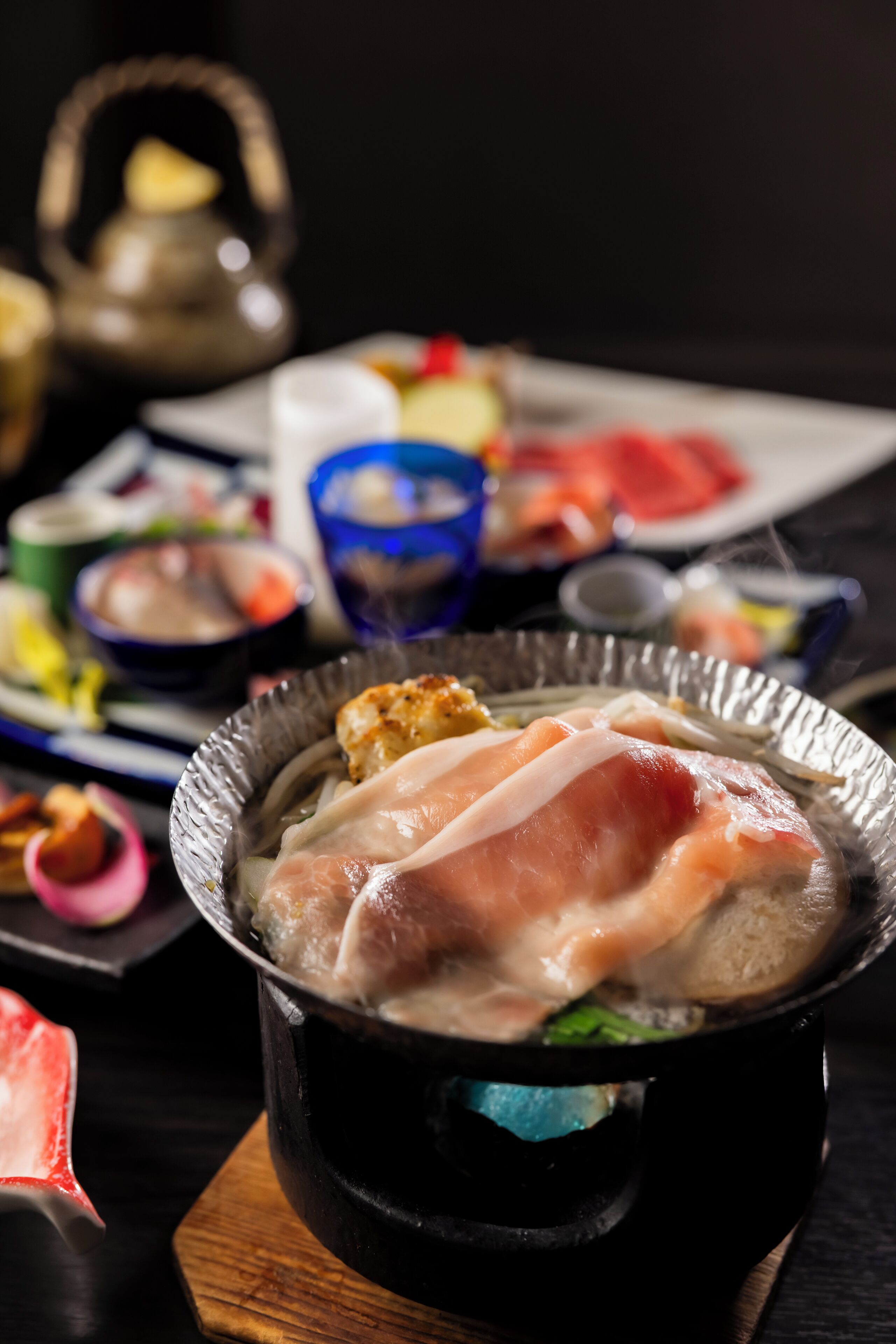 A hot pot with meat and vegetables, a teapot, and various dishes on a table.