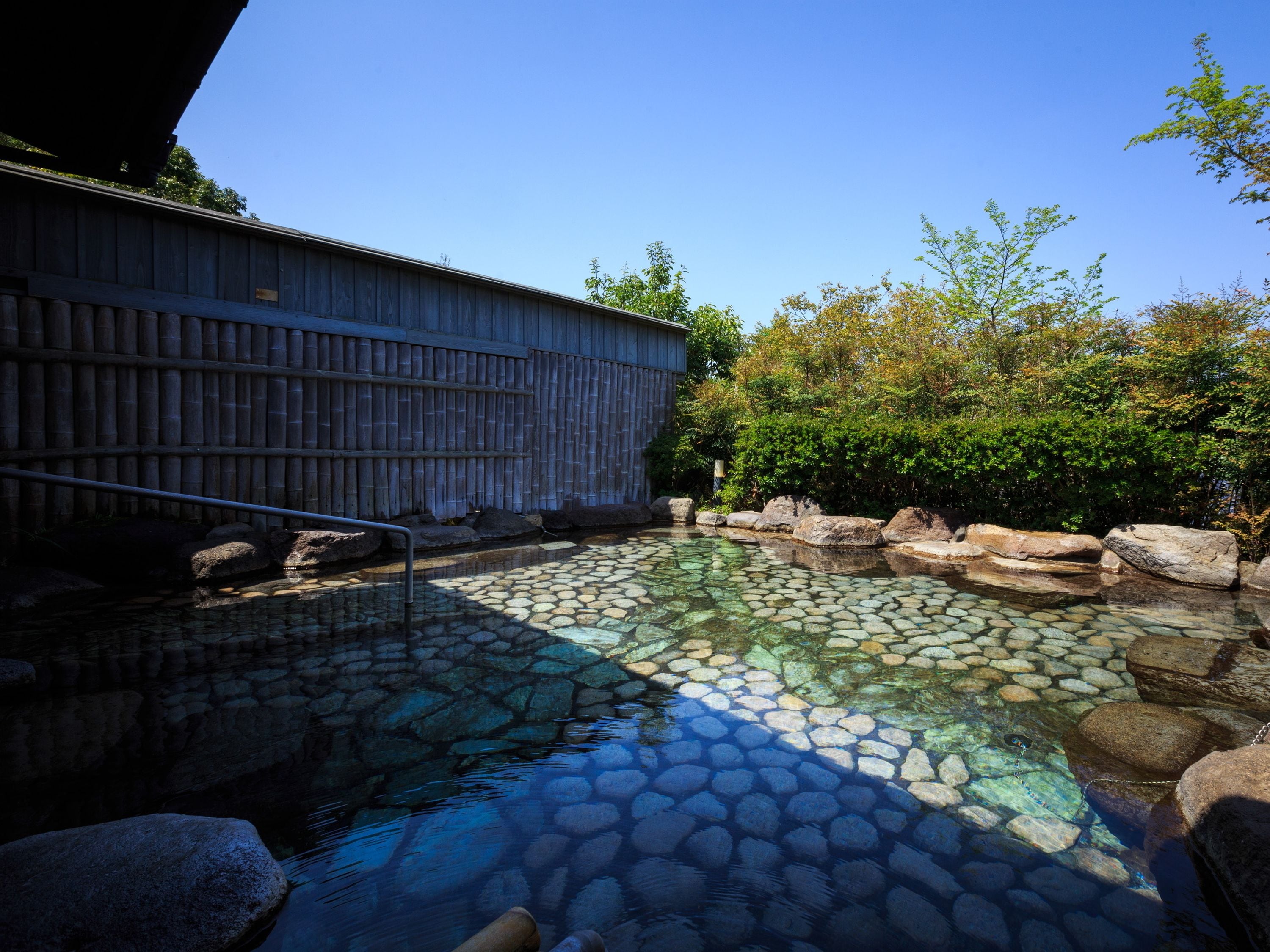 A stone pool with a wooden fence and rocks, surrounded by greenery.
