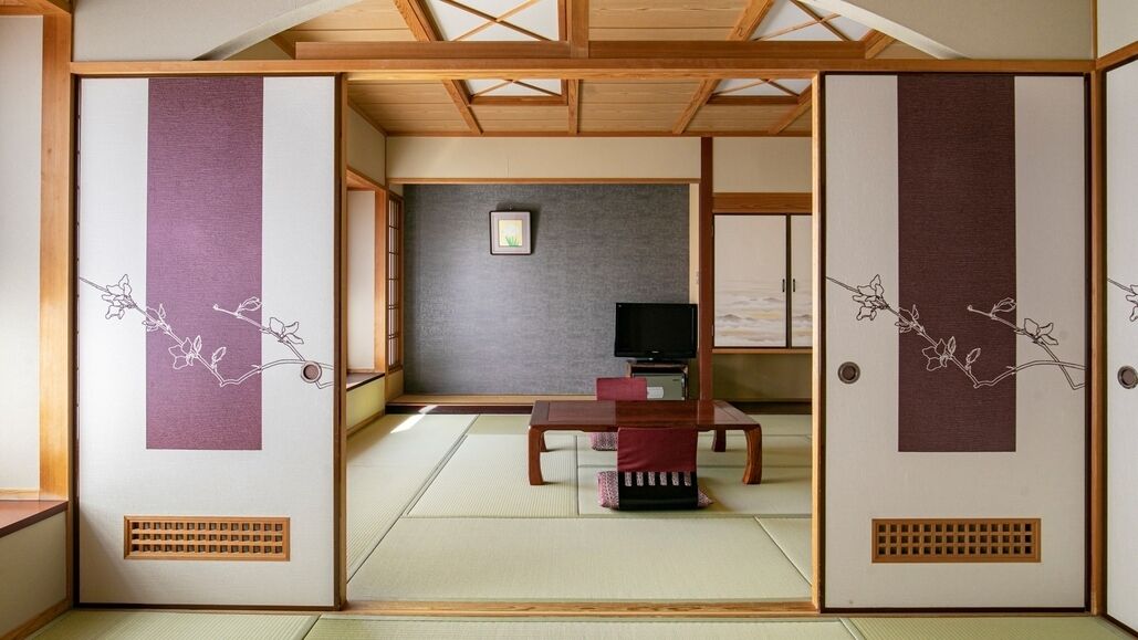 A traditional Japanese room with tatami flooring, a television, and a low table with a red cushion.