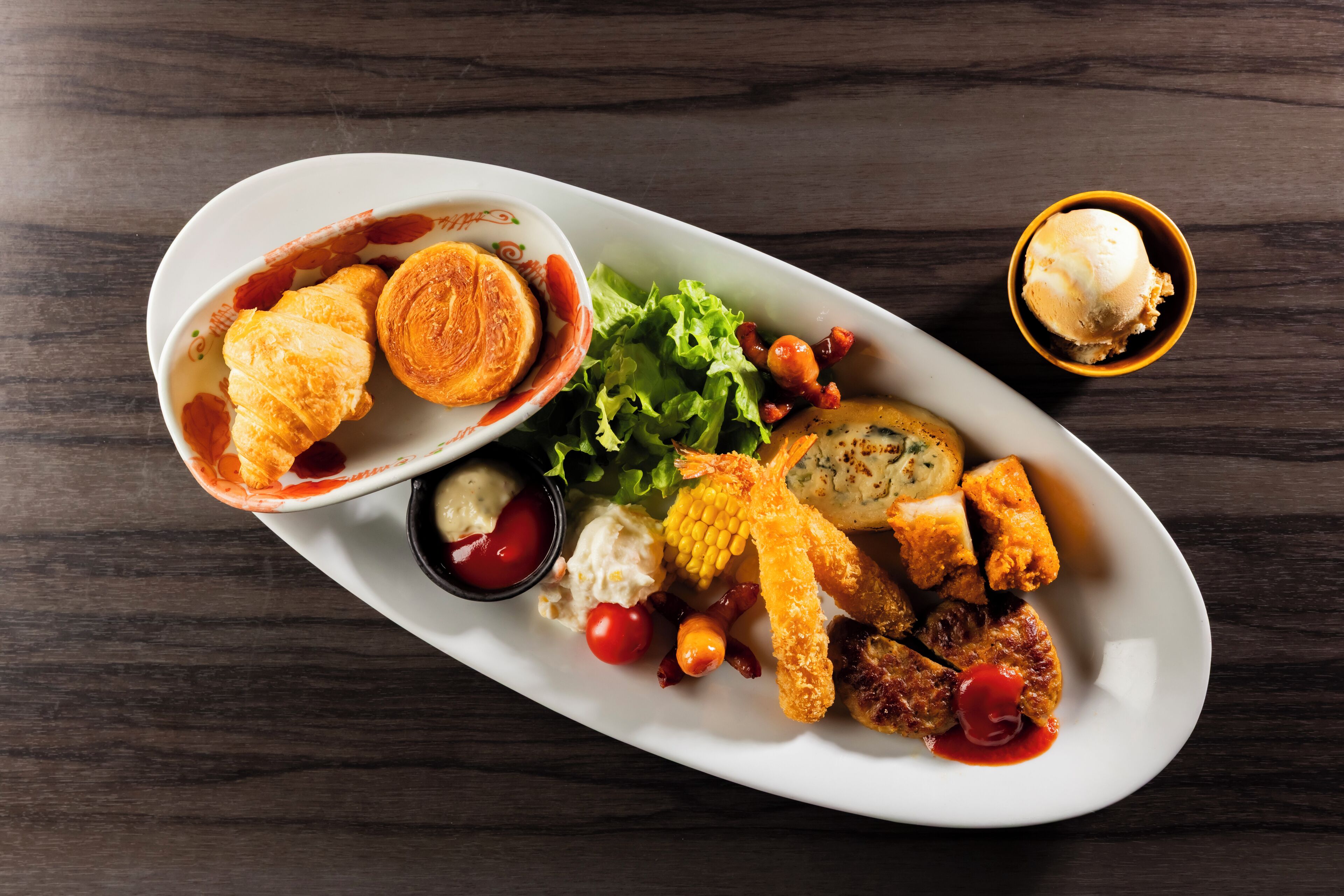 A white oval plate with various food items including fried chicken, corn, and a small bowl of sauce.
