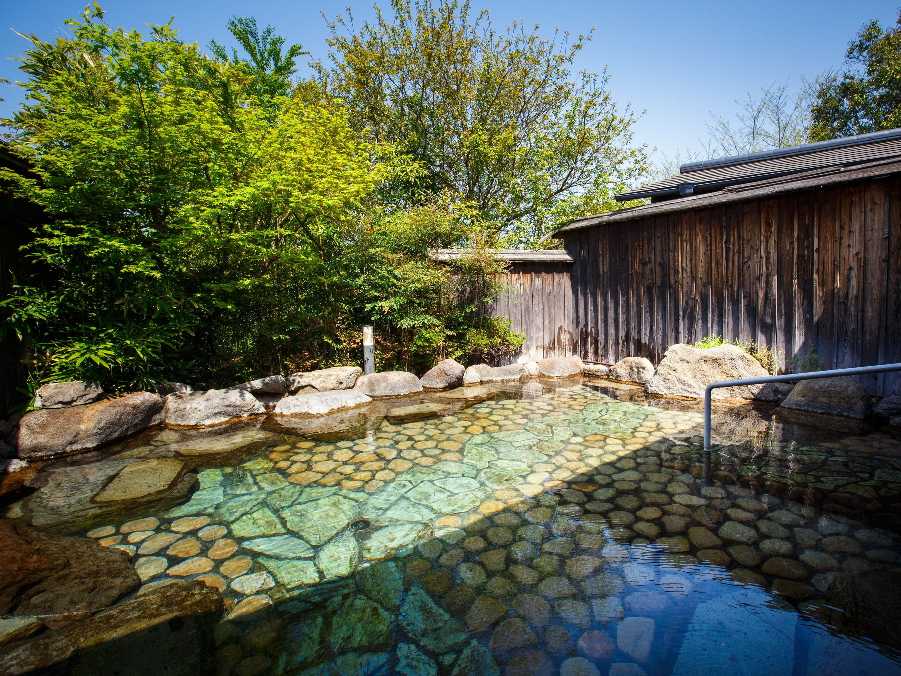 A traditional Japanese onsen with a stone bath surrounded by rocks and greenery.
