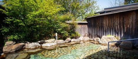 A traditional Japanese onsen with a stone bath surrounded by rocks and greenery.