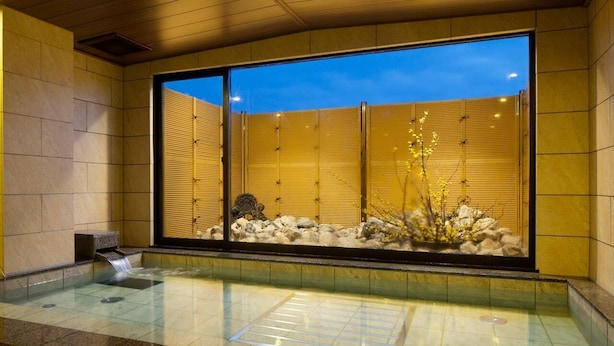 A traditional Japanese onsen with a view of the night sky through sliding doors, a stone bath, and a small waterfall feature. - Futabaso (Hikone)