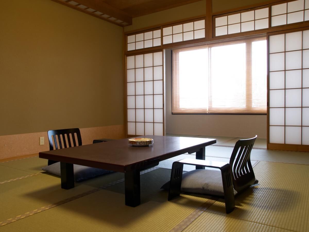 A traditional Japanese room with tatami flooring, a low table, and two chairs.