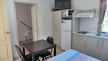 Een compacte keuken met een magnetron, koelkast en een klein spoelbakje. Er staat een eettafel met stoelen en een tafelkleed met een patroon.
