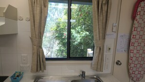 Una cocina con un lavamanos de acero inoxidable, una ventana con cortinas y un escurreplatos azul.