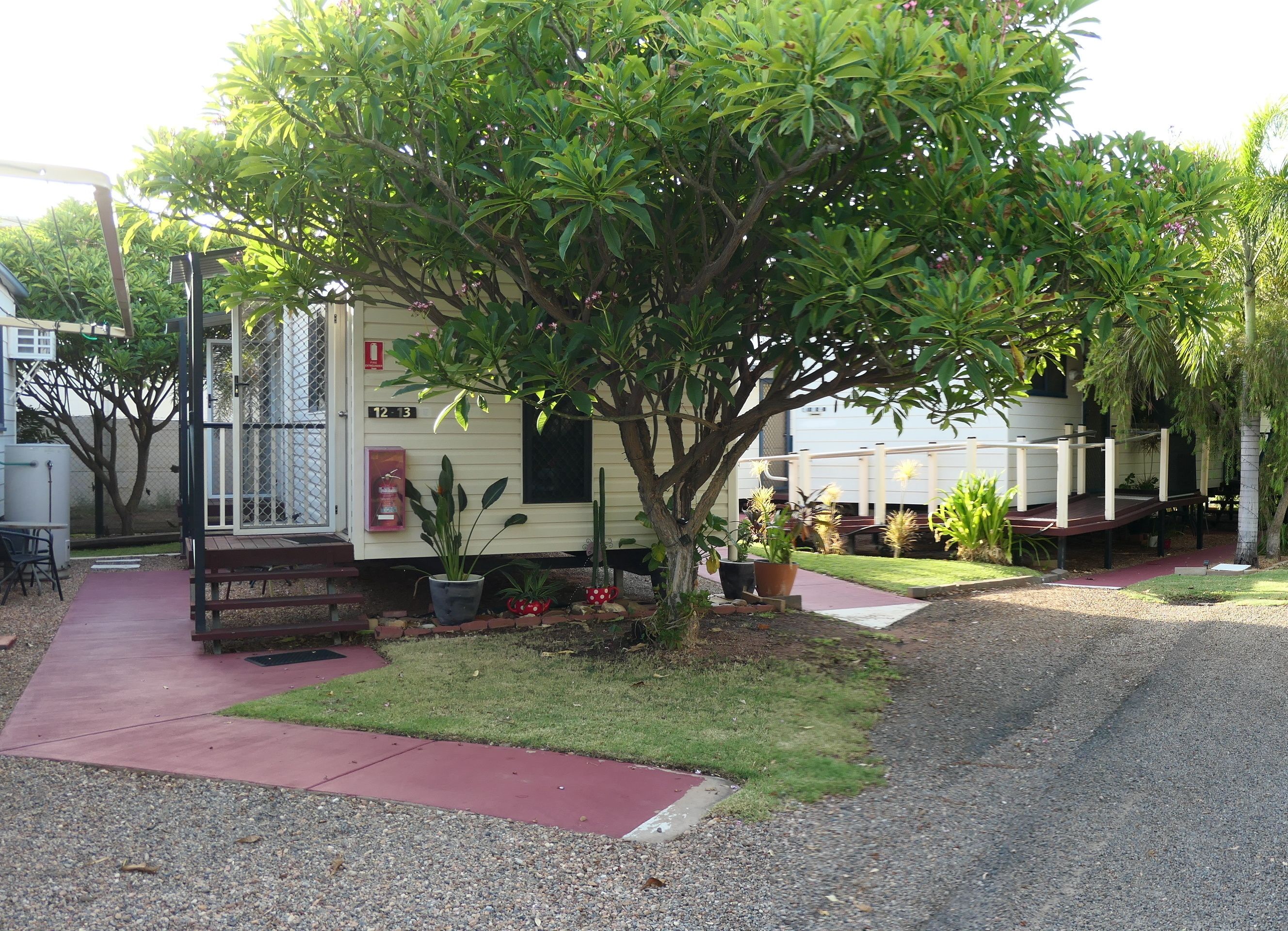 A mobile home with a small garden area, a fire extinguisher mounted on the wall, and a paved walkway.