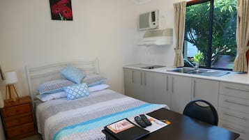 Quarto com cama, escrivaninha com um caderno, cadeira, mesa de cabeceira, janela com cortinas, pia e armários.