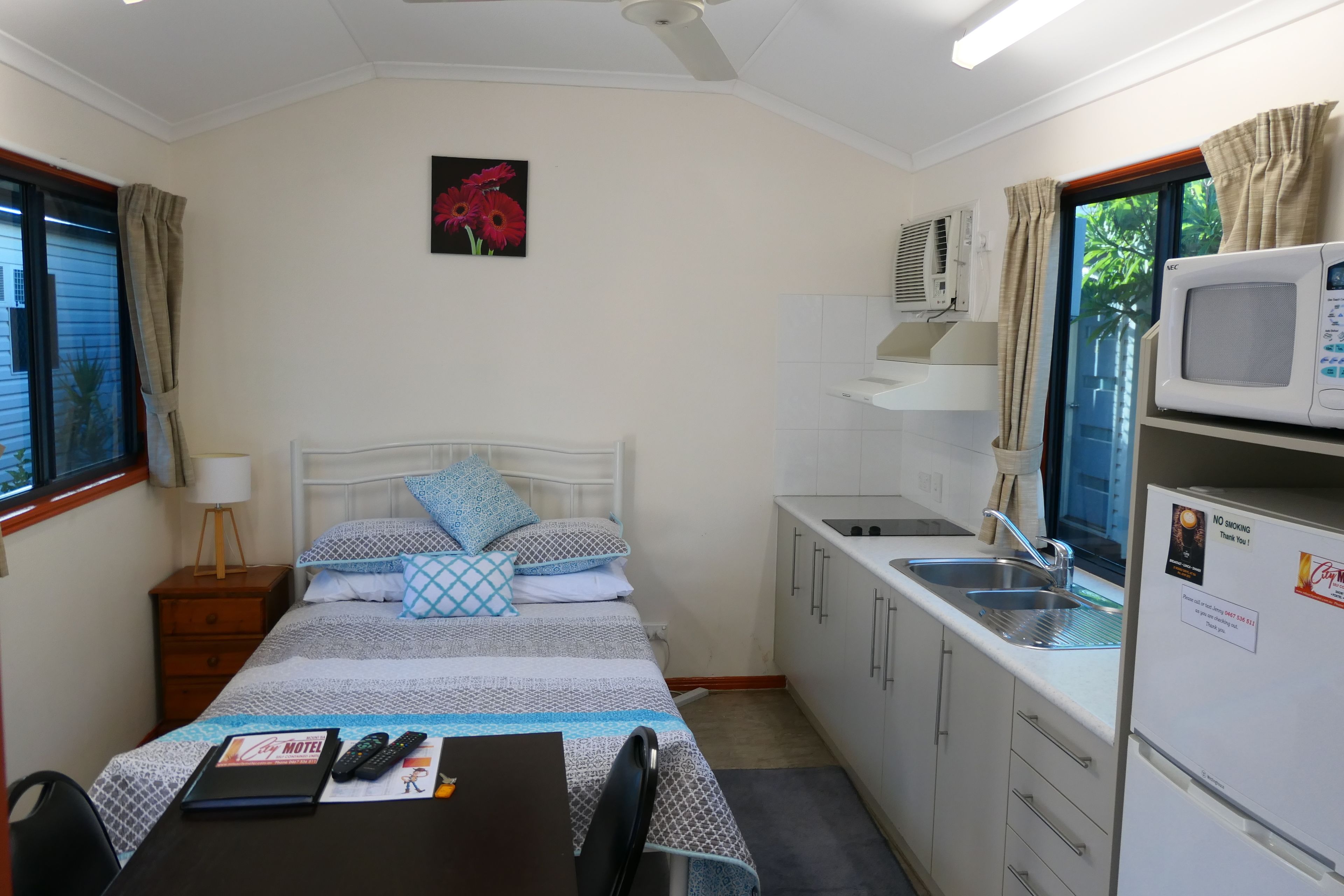 Una habitación de hotel compacta con una cama individual, un pequeño kitchenette, una mesa de comedor y un ventanal con cortinas.