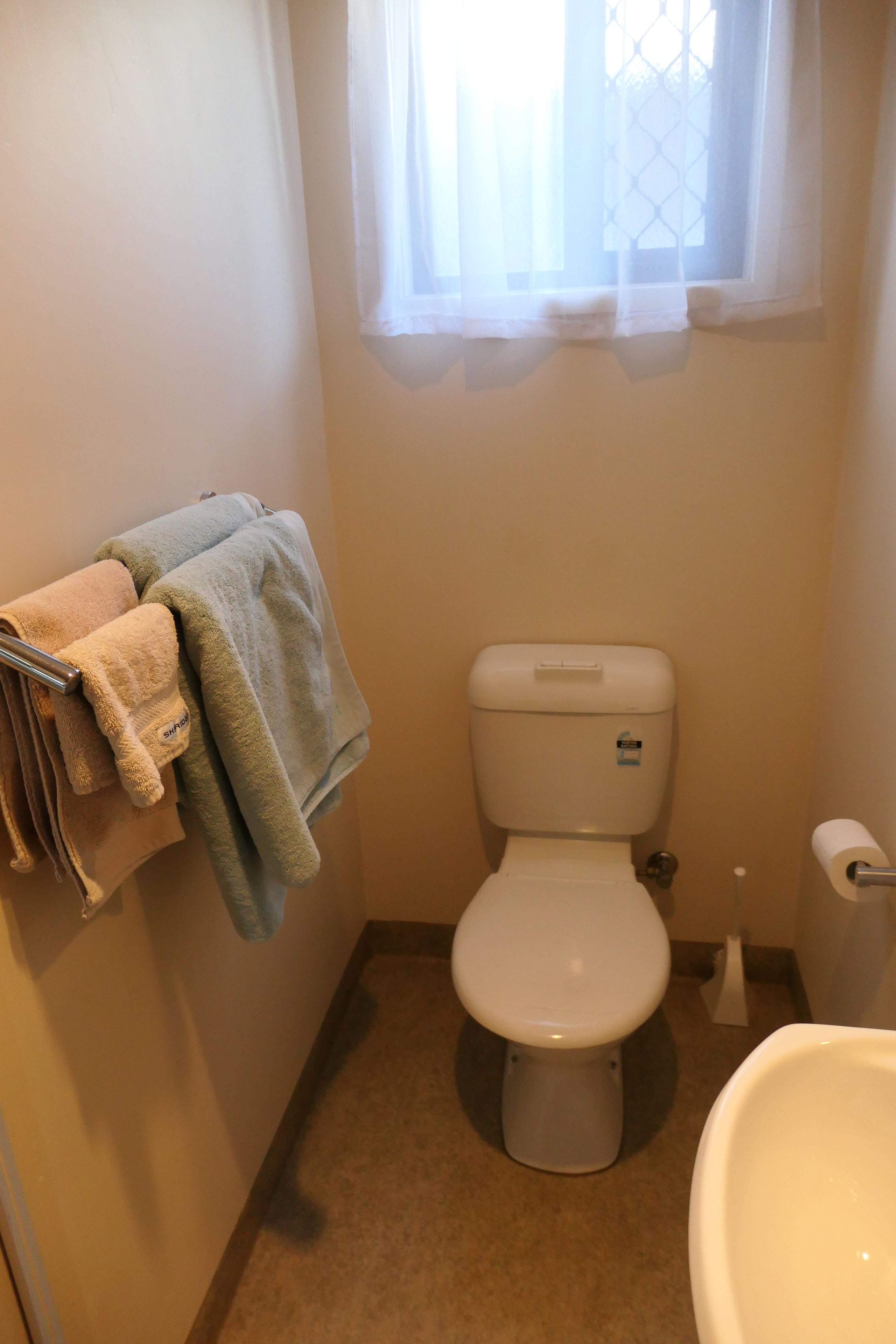 A small bathroom with a toilet, a sink, and a towel rack with folded towels.