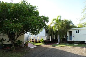 Una casa móvil con un porche, rodeada de plantas en macetas y un gran árbol.