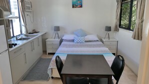 Un dormitorio pequeño con cama, mesitas de noche, escritorio y una silla.