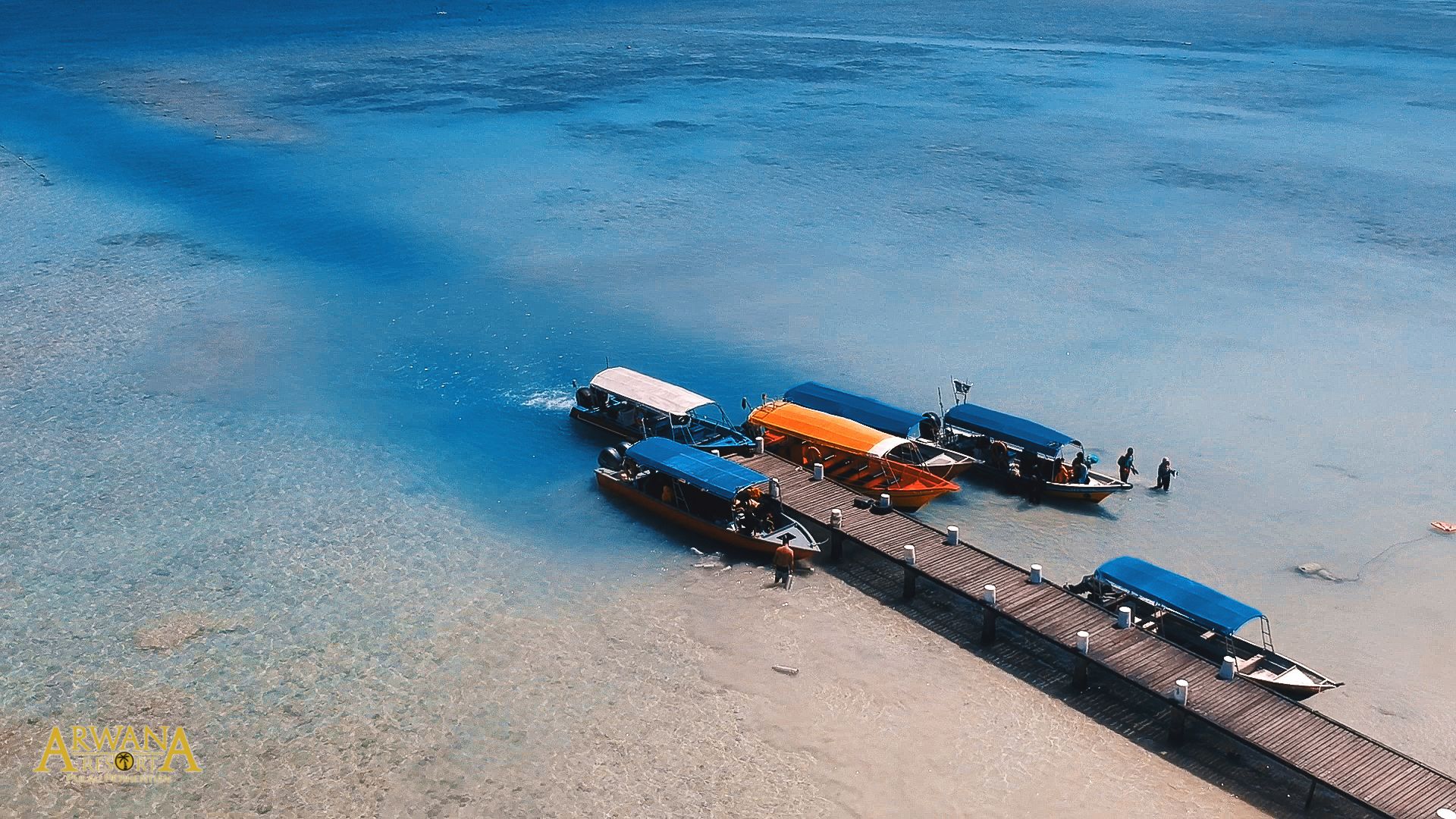 Un muelle con varias embarcaciones, una playa de arena y aguas azules cristalinas.