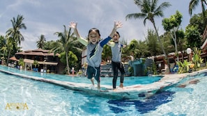 Two children playing in a pool with palm trees and a building in the background.