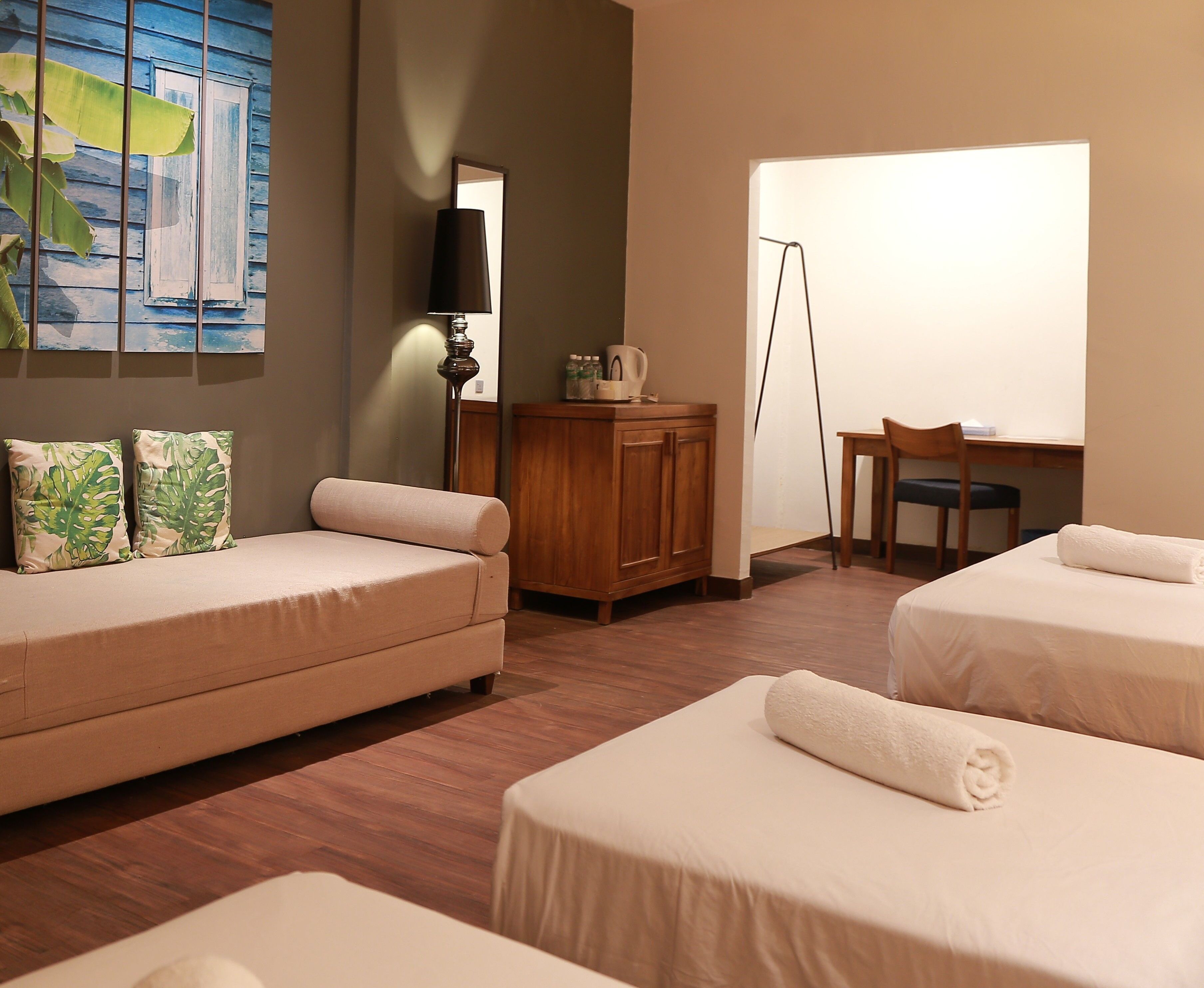 A hotel room with a sofa, two beds, a wooden cabinet, a desk, and a large window.