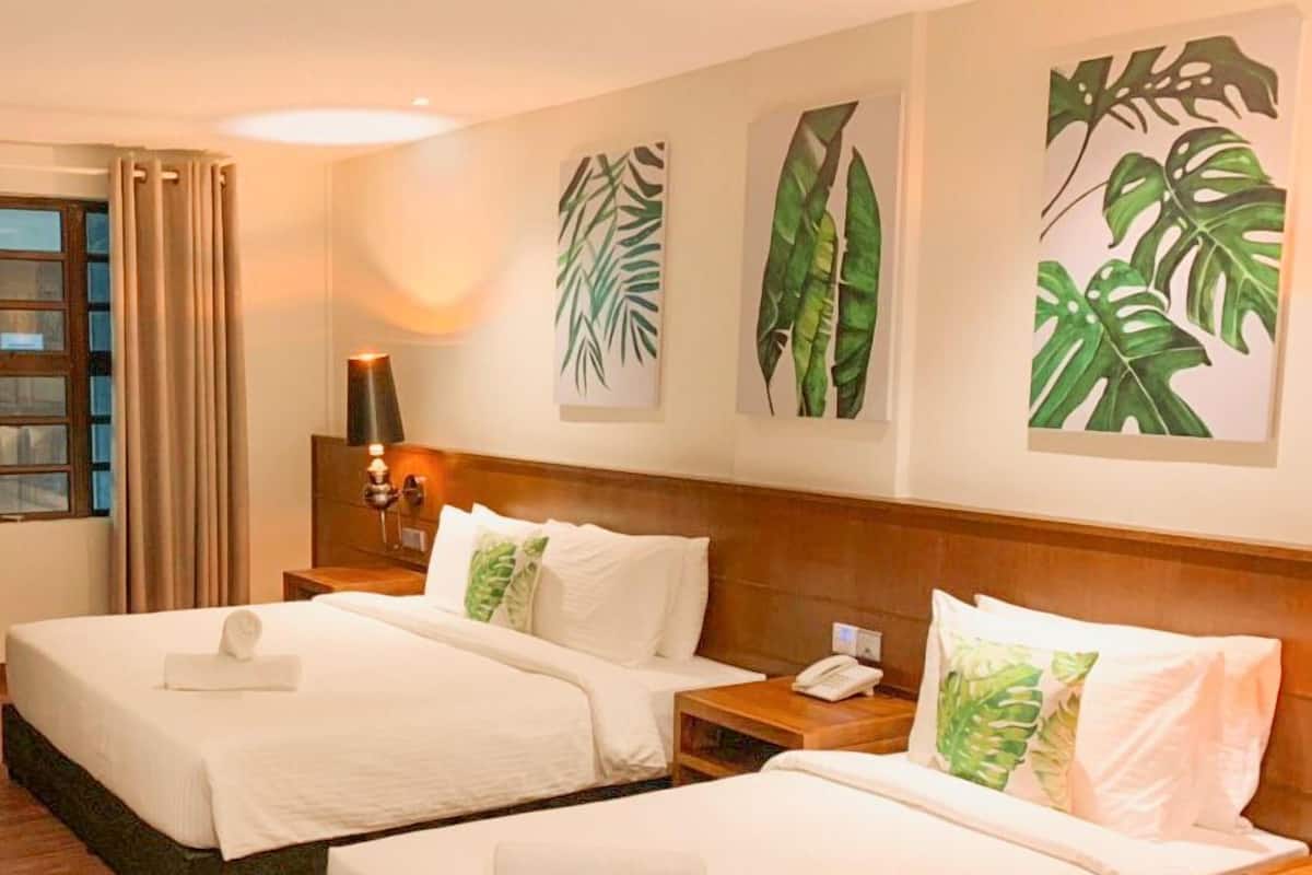 Ein Hotelzimmer mit zwei Betten, einem hölzernen Kopfteil, einem Nachttisch mit Telefon und Wandbild mit tropischen Blättern.
