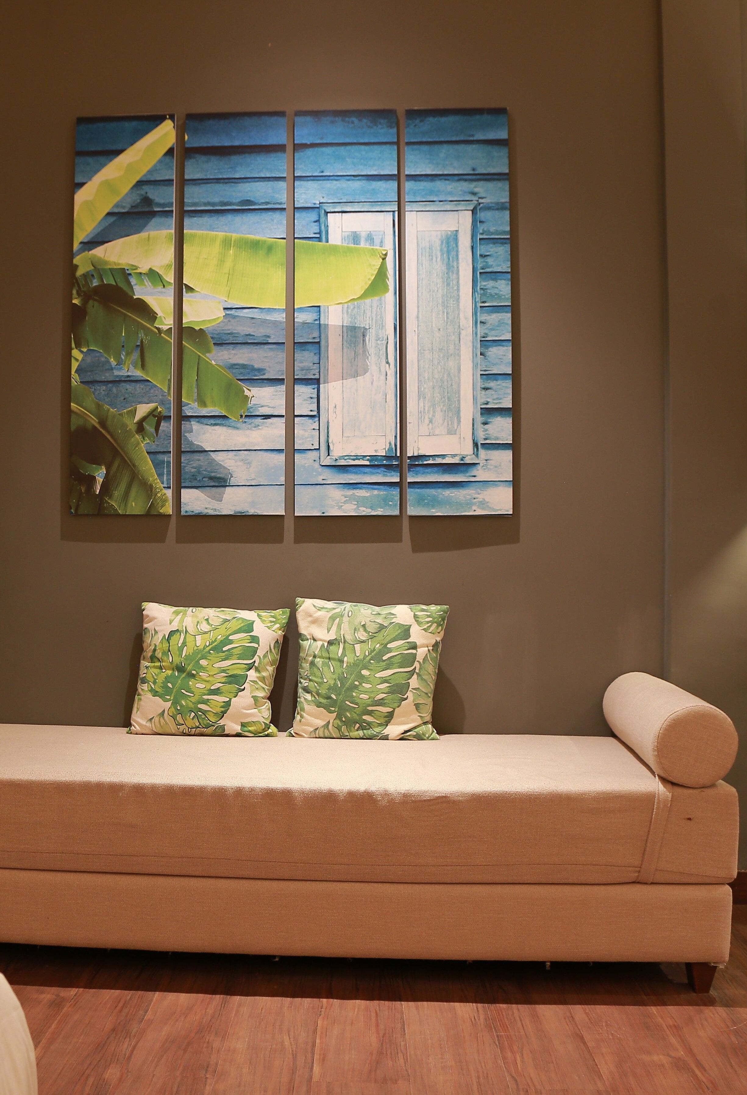 A beige sofa with two patterned pillows against a wall with a tropical-themed painting.
