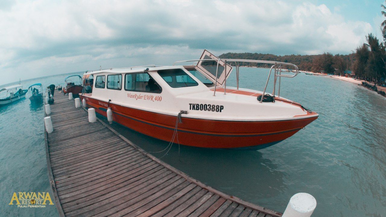 Un barco rojo y blanco amarrado a un muelle de madera, con vistas a una playa y árboles al fondo.