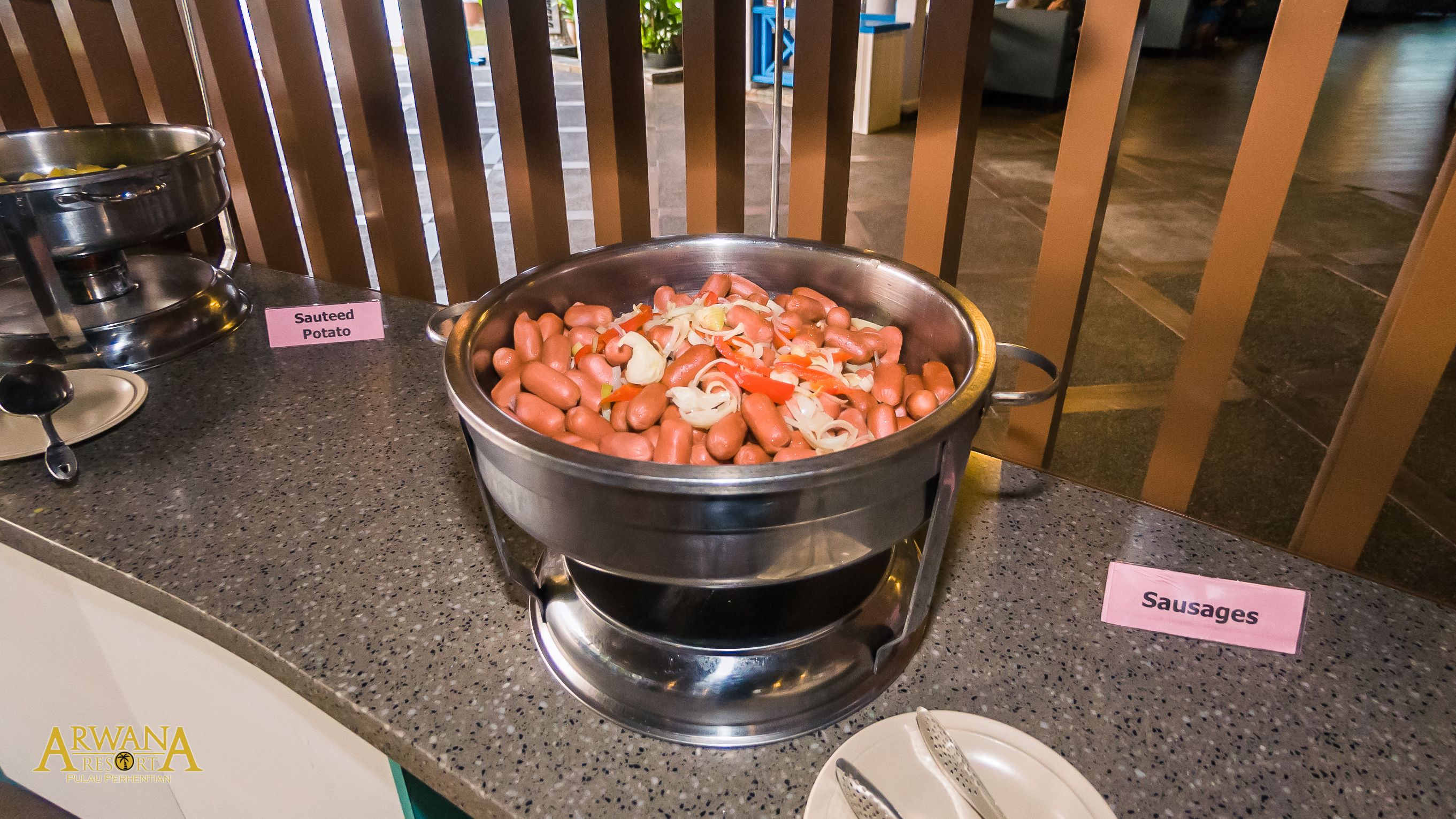 A buffet with a pot of sausages and a pot of sauteed potatoes.