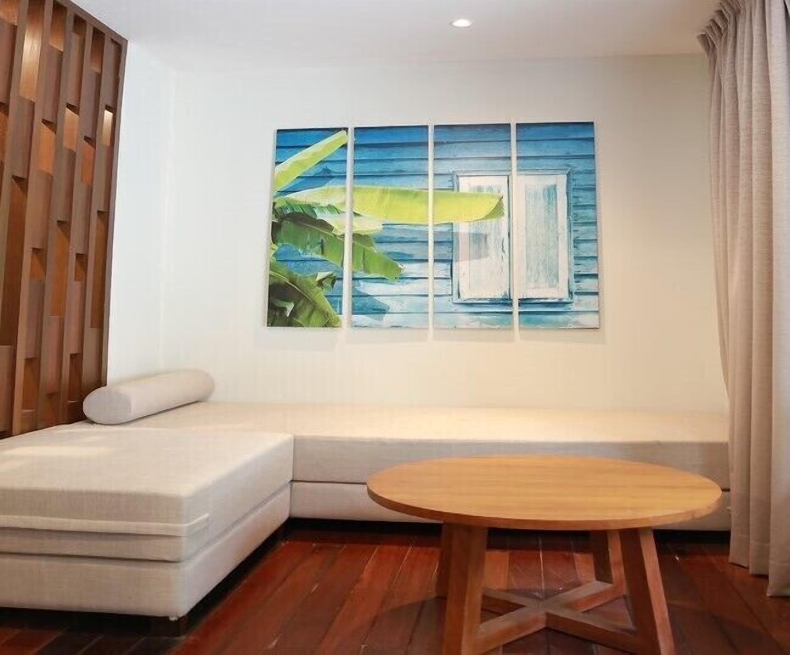 A room with a sectional sofa, a round wooden table, and a large painting on the wall.