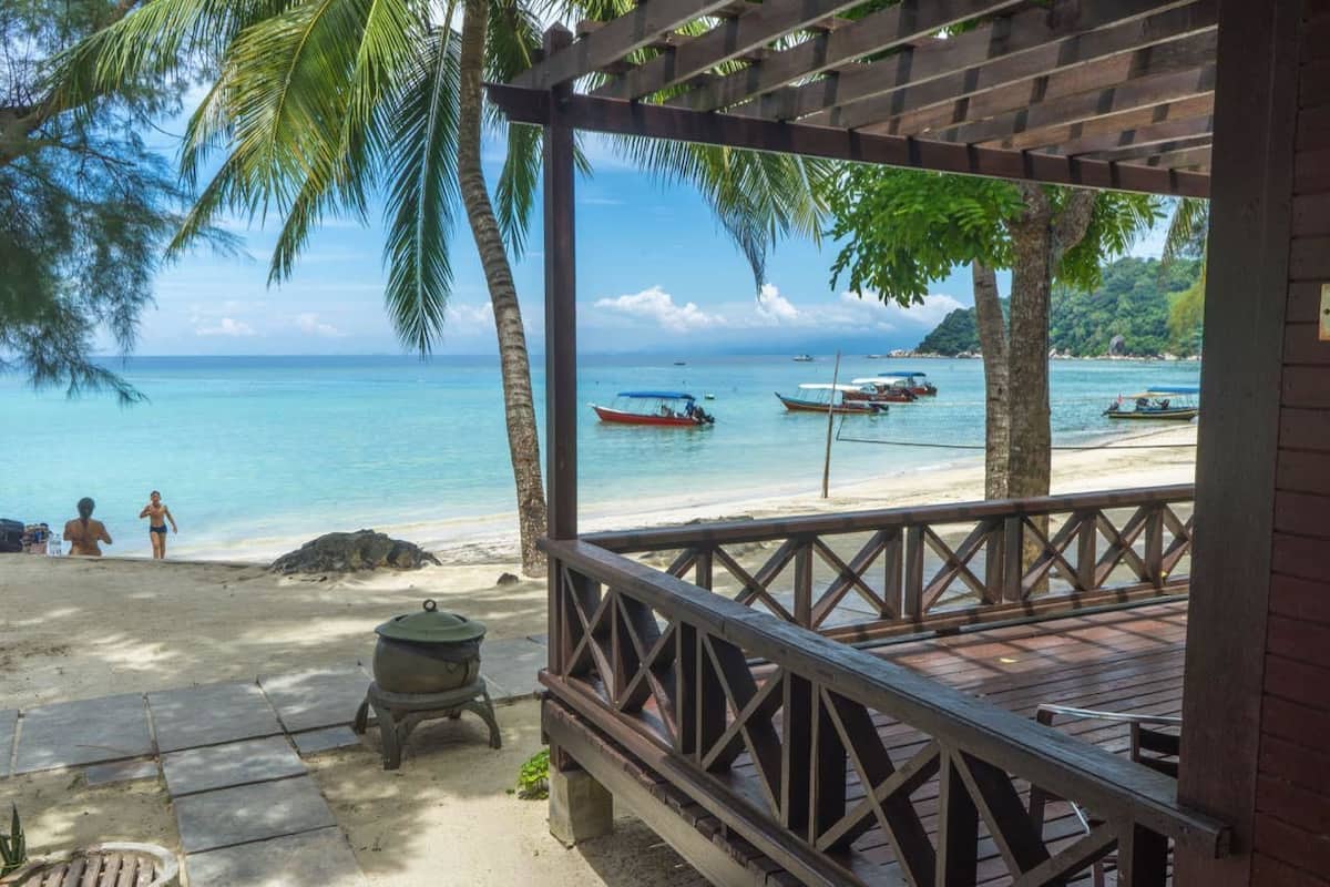 Blick auf einen Strand von einer Holzdielen-Terrasse mit Grill und Meer sowie Booten.