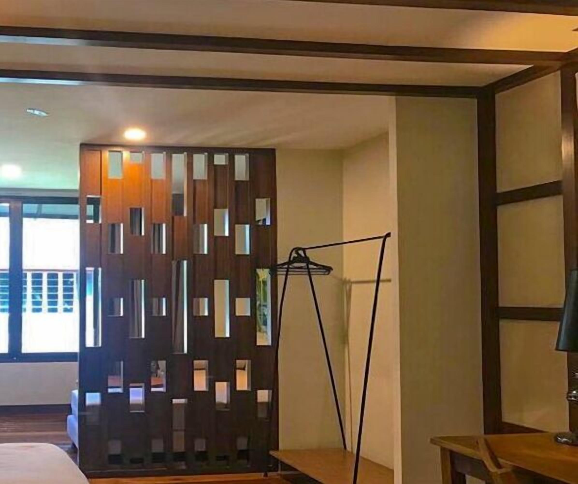 Una habitación de hotel con un separador de madera, una cama, un escritorio y una lámpara.