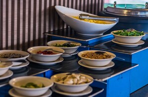 A buffet table with various dishes, including pasta, salad, and other prepared foods, set against a striped wall. - Arwana Perhentian Eco & Beach Resort (Pulau Perhentian Besar)