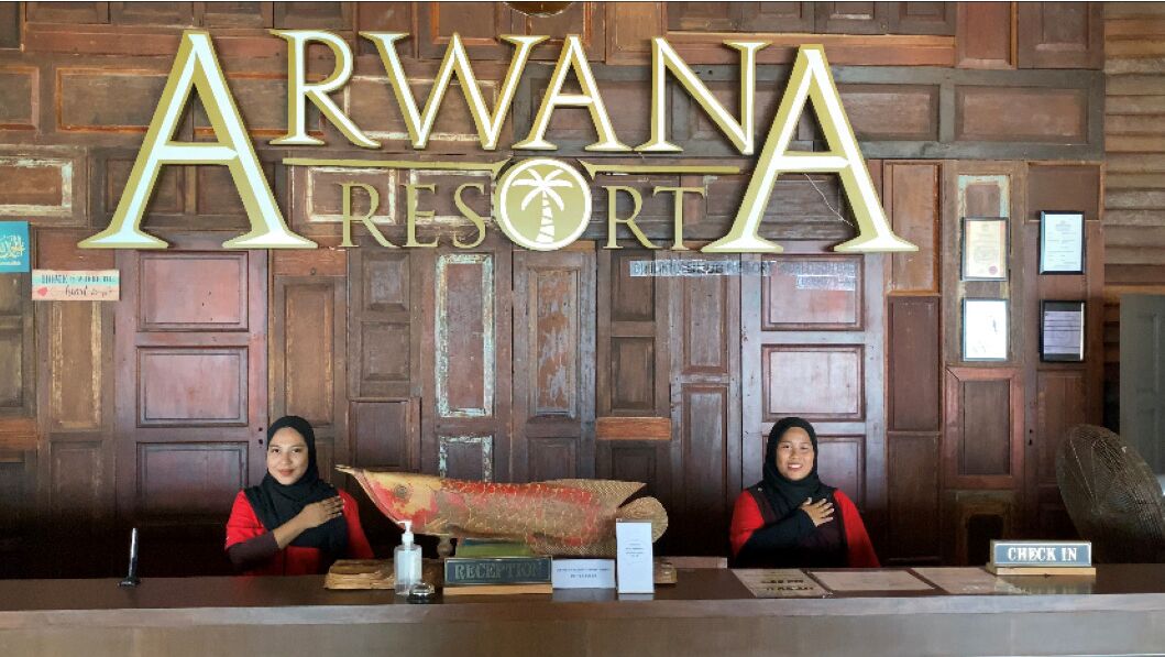 A reception desk at Arwana Resort with wooden paneling and a large sign above.