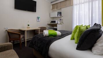 A hotel room with a bed, a desk, a chair, a television, a microwave, and a window with curtains.