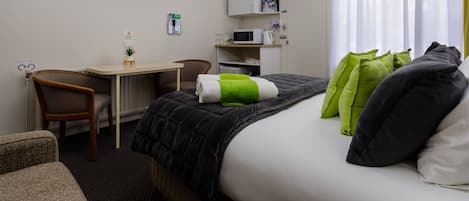 A hotel room with a bed, a desk, a chair, a television, a microwave, and a window with curtains.