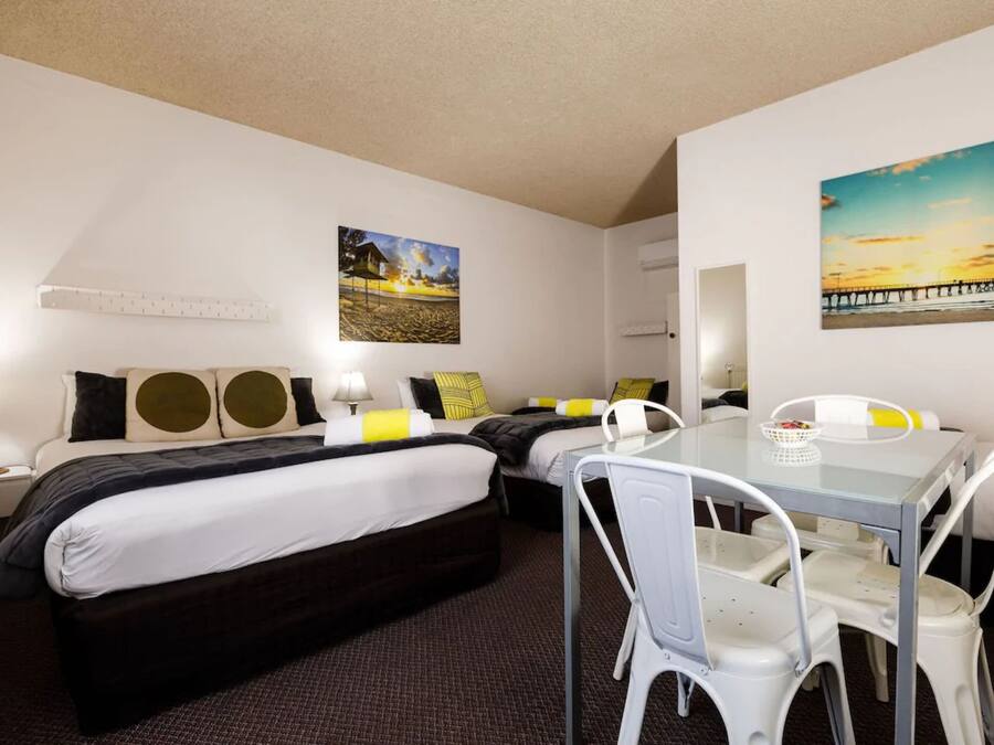 A hotel room with two beds, a dining table with chairs, a mirror, and two paintings on the walls.