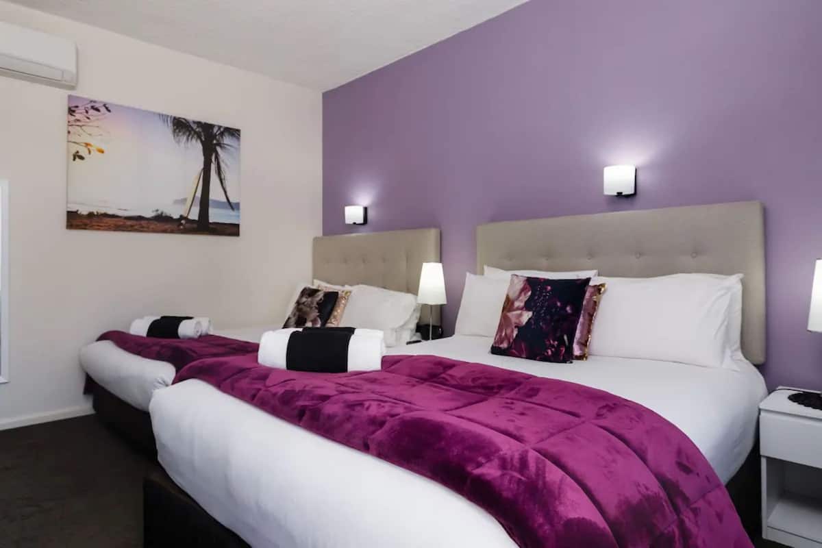 A hotel room with two beds, purple walls, and a beach-themed painting.