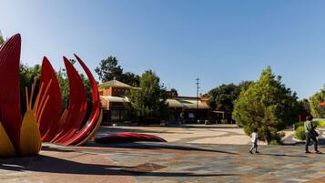 A plaza with large red and yellow sculptures, a building with a green roof, and a clear blue sky.