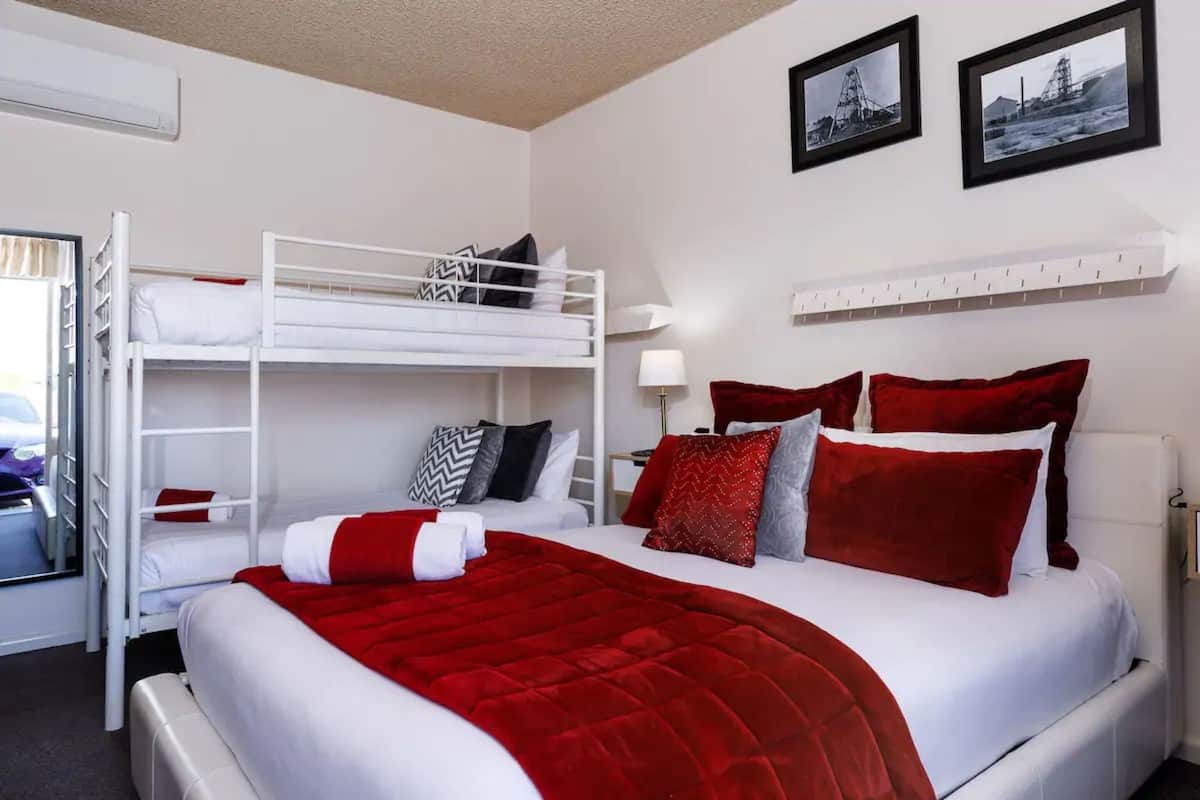 A hotel room with a bunk bed, a red and white bedspread, and two framed pictures on the wall.