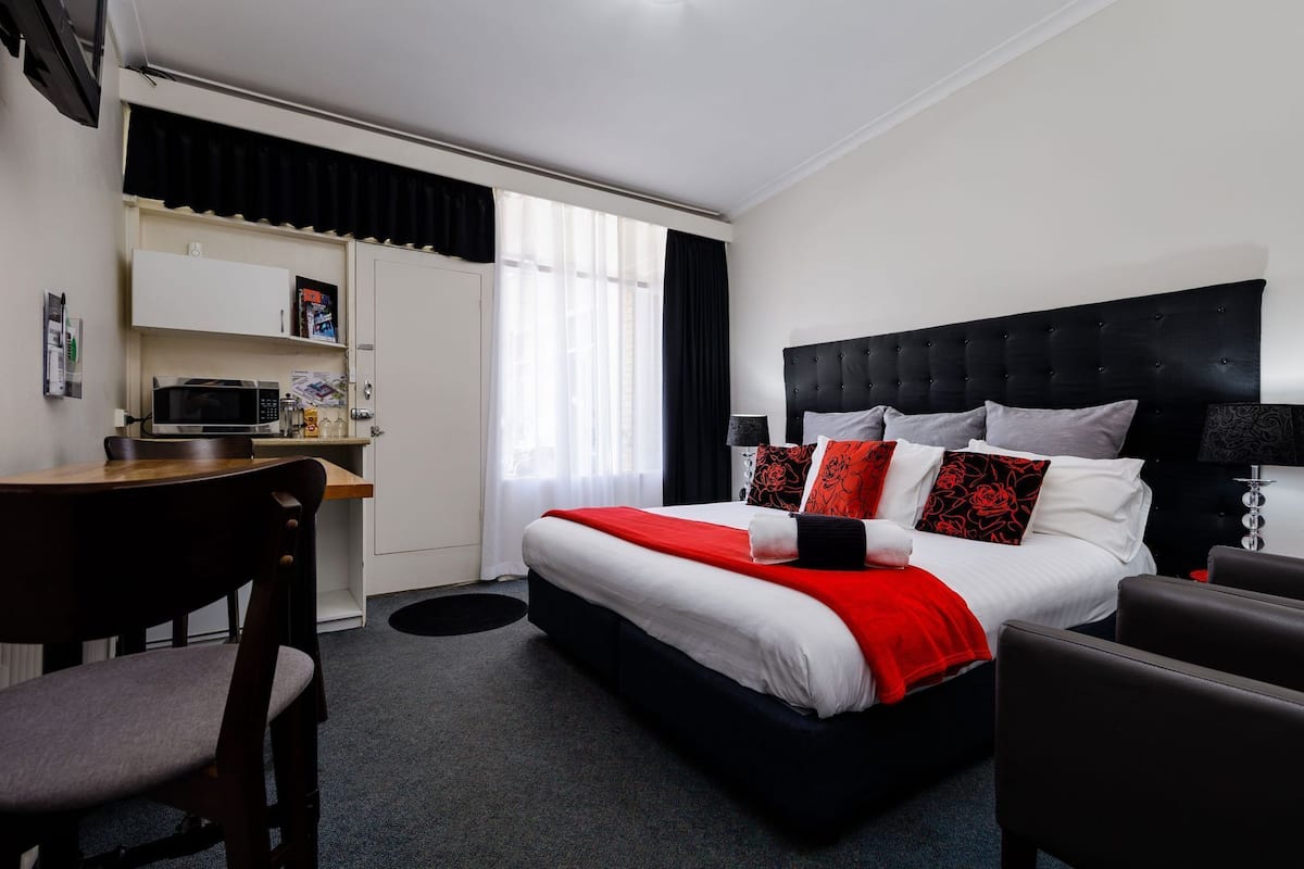 A hotel room with a bed, a desk, a chair, a microwave, and a window with curtains.