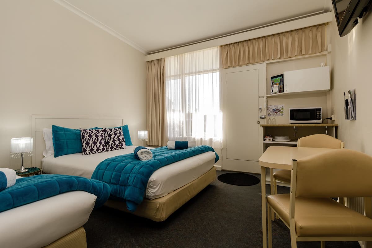 A hotel room with a bed, a desk, a chair, a microwave, and a small cabinet.