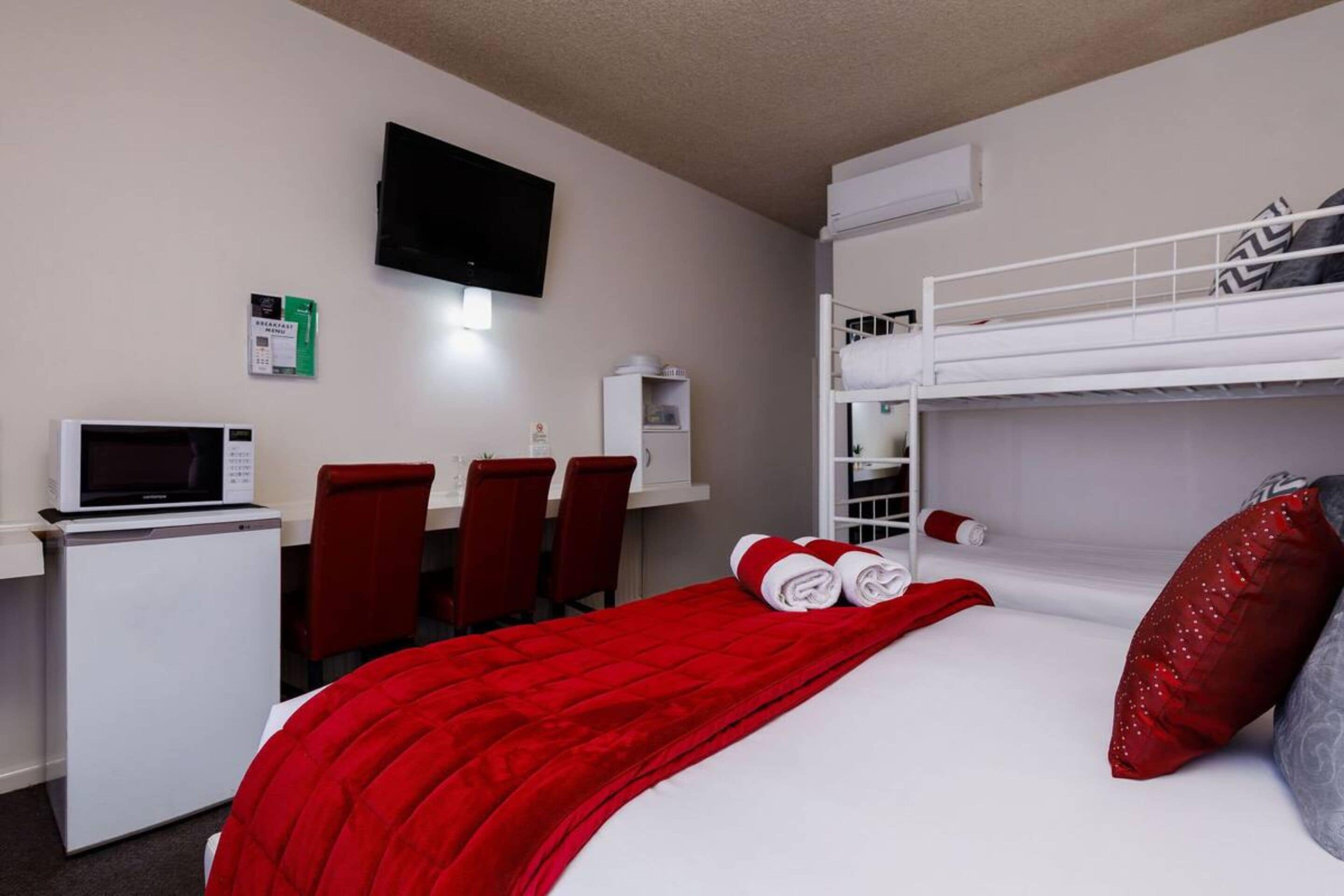 Quarto de hotel com uma cama beliche, uma mesa com computador, micro-ondas e televisão.