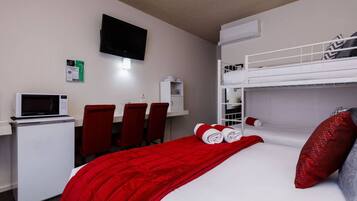 Quarto de hotel com uma cama beliche, uma mesa com computador, micro-ondas e televisão.