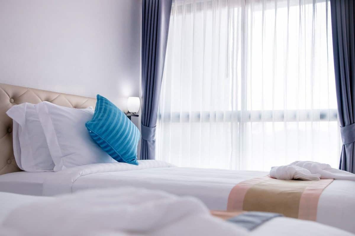 Un lit bien fait, avec des oreillers blancs et bleus, une tête de lit beige et une couverture blanche.