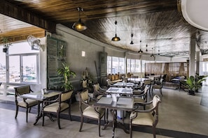 Un restaurant spacieux, doté de hauts plafonds et baigné de lumière naturelle, avec des meubles en bois et des plantes en pot.