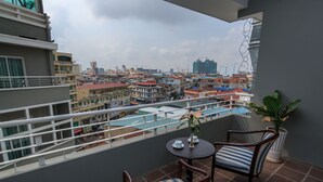 A balcony with a view of a cityscape, including buildings and construction cranes. There are two chairs and a small table with a vase and a cup. - Paradise Hotel (Phnom Penh)